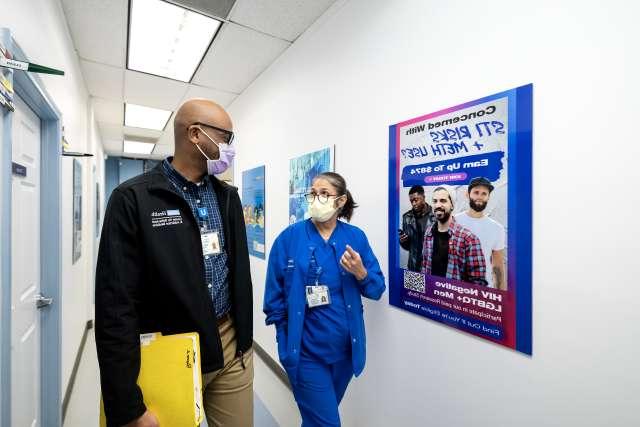 临床研究员Christopher Blades和实验室协调员Demetria Villanueva走在Vine Street诊所的走廊上.
