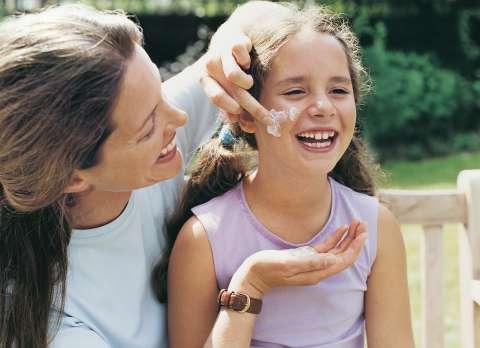 Woman putting lotion on girl's cheek